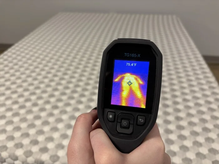 A closeup of someone pointing a thermal gun at the soft side of the Layla to take its temperature after someone has rested on it for 5 minutes. The screen reads 75.4 degrees.