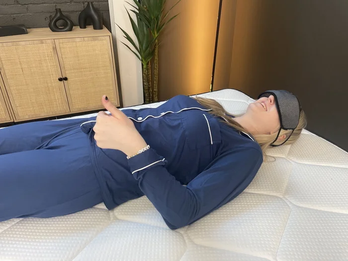 A woman lying on the Plank Firm mattress while wearing an eye mask. She's giving a thumbs-up to indicate that she can feel her partner moving around.