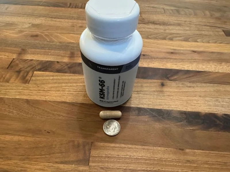 A capsule of Transparent Labs KSM-66 Ashwaganda Extract is shown next to a dime for size comparison.
