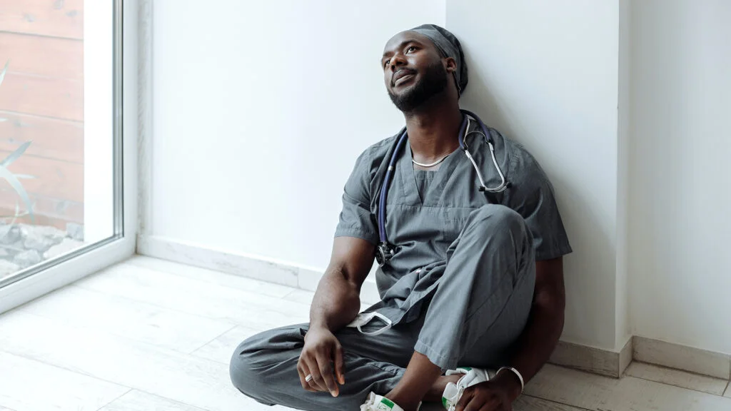 A male doctor leaning against the wall, looking tired during his shift.