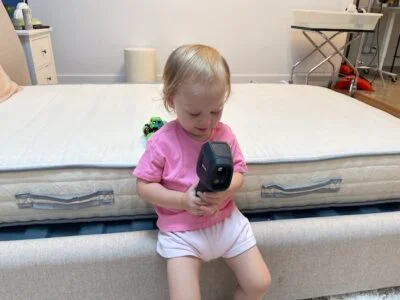 A toddler leaning against the Nolah Nurture mattress and playing with a temperature reader.