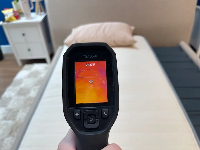 A closeup of a thermal gun reading the temperature of the Nolah Nurture mattress. The temperature is at neutral, with the screen displaying 76.5 degrees.