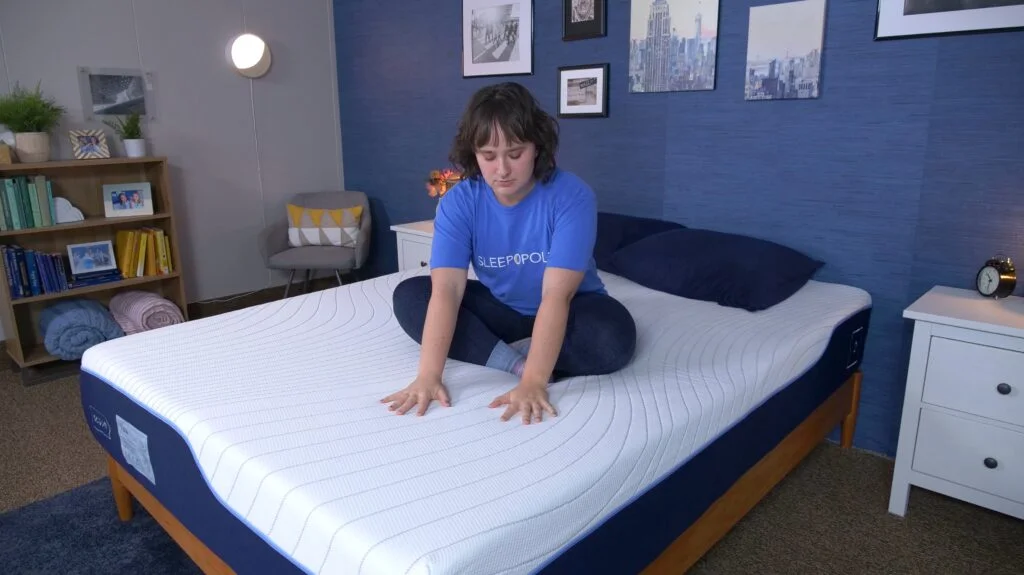 A woman sitting crosslegged on the Octave Vista mattress and pressing into its cover.