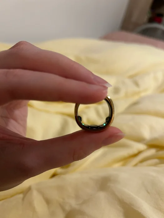 A hand holds up the RingConn ring, showing off two green lights on the inner hardware.