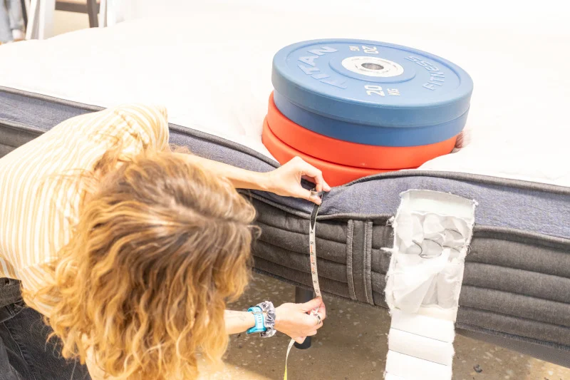 Our tester measures the compression of weight plates to assess edge support on a Helix Midnight Luxe Mattress mattress.