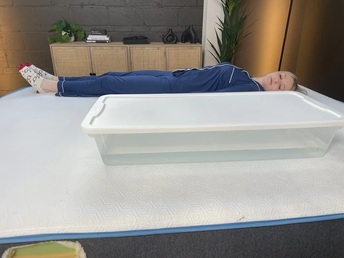 A woman lying next to a bin full of water on the Bear Original mattress. She's seeing how much the water moves with her to measure the bed's motion isolation.