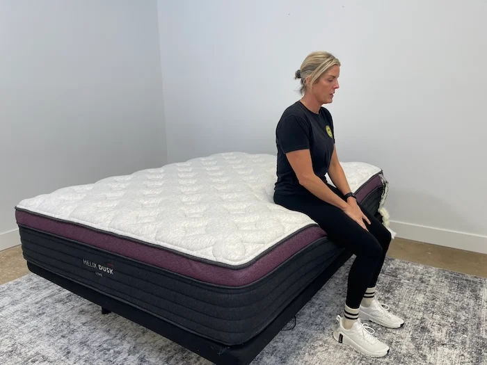 A woman sitting on the edge of the Helix Dusk Luxe mattress.