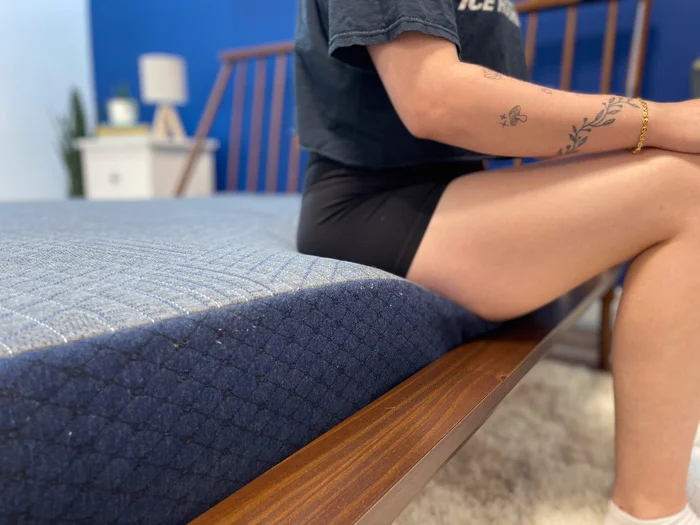 A close-up of a woman sitting on the edge of the BB Kids mattress.