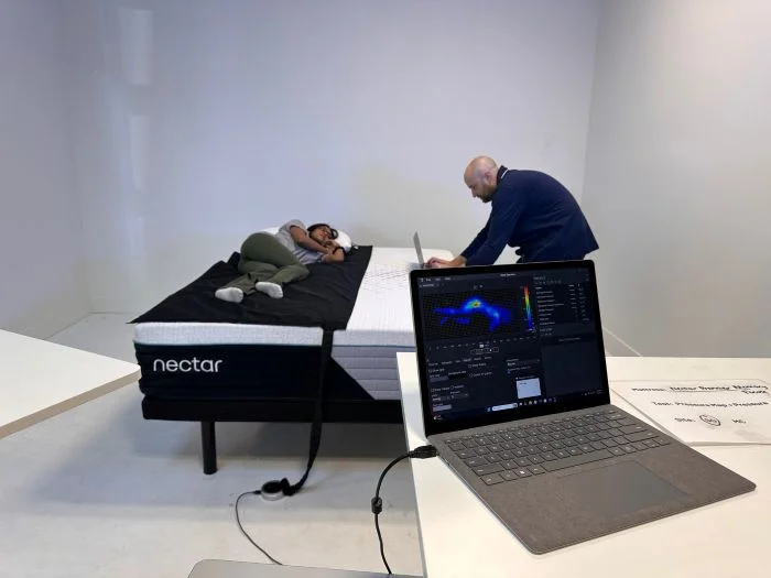 A woman lies on a pressure mat on the Nectar Premier mattress as a man types on his laptop on the other side of the bed
