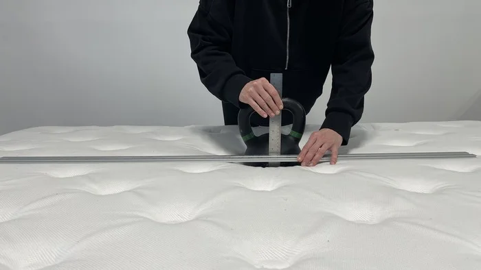 A kettlebell resting on the surface of the WinkBed. Someone is standing next to it and measuring the sinkage with a ruler.