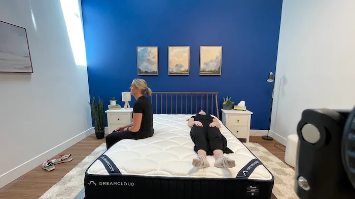 A woman sits on the edge of the DreamCloud mattress while another woman lies next to her.