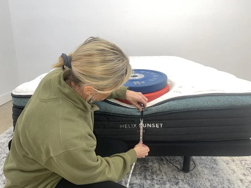 Our tester measuring weight plates on the edge of the Helix Sunset Luxe Mattress