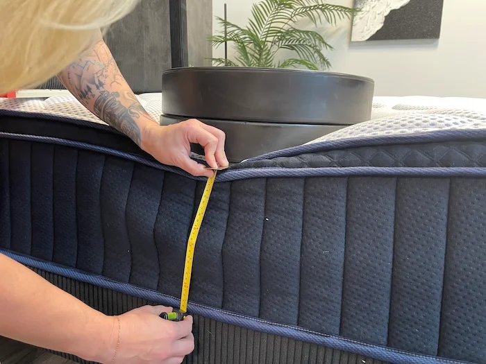 A closeup of a stack of weights resting on the DreamCloud Premier Hybrid mattress. A woman is measuring the sinkage with a tape measure.