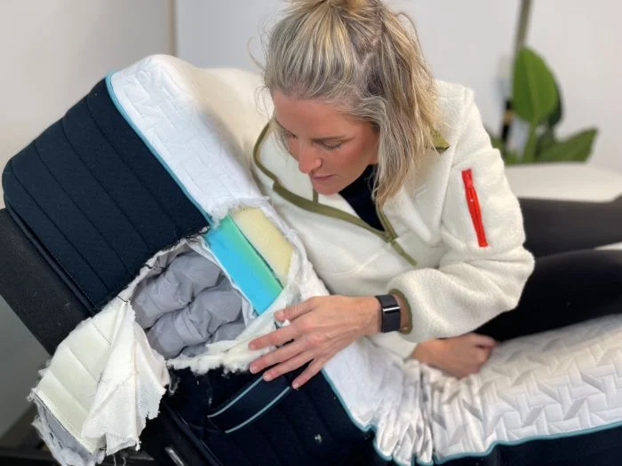 A woman inspects the inner layers of the Nectar Premier mattress while sitting up on the bed, which is placed on an adjustable base