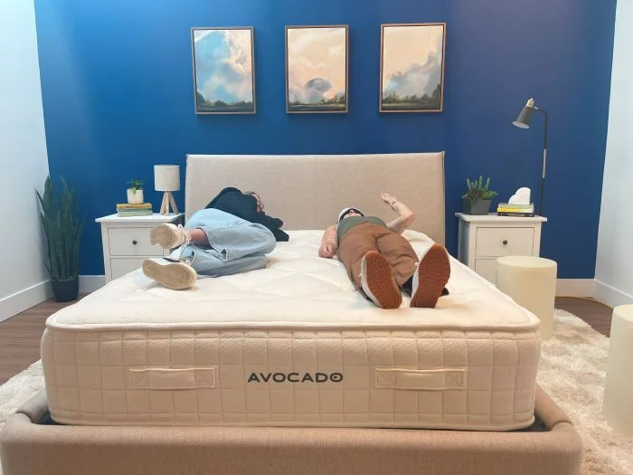One woman lies on an Avocado Luxury Organic mattress while another one rolls around next to her.