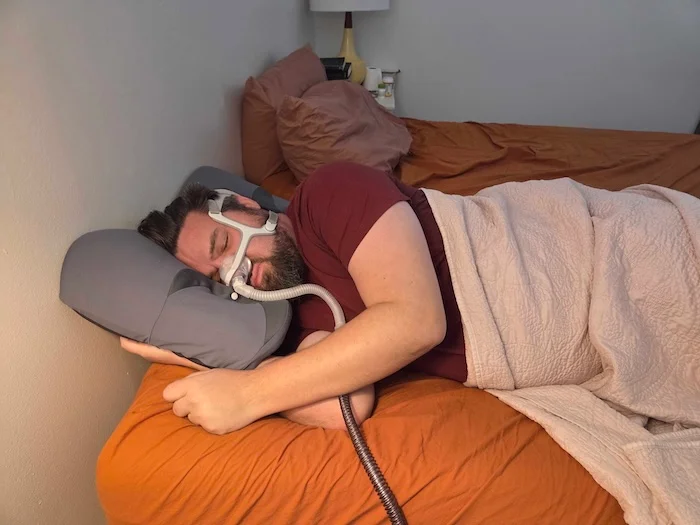 A man sleeping on his side on the Ikstar pillow. He's wearing a sleep apnea mask as he dozes.
