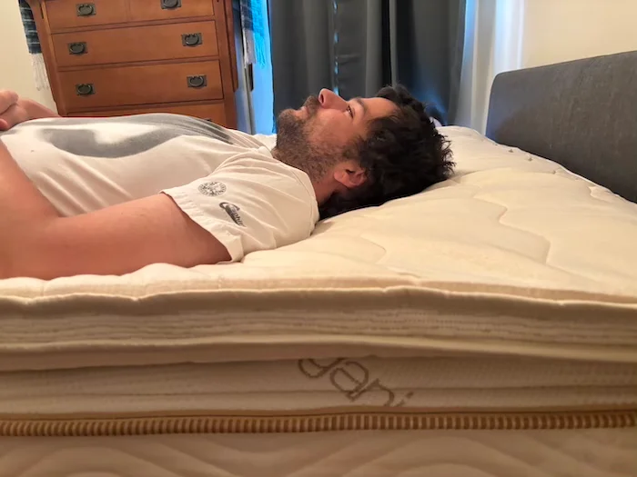 A man lying on his back on the Saatva Organic Quilted Topper.