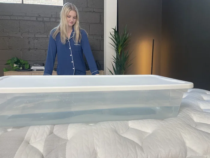 A woman staring at a plastic bin full of water on the Leesa Sapira Chill Hybrid.