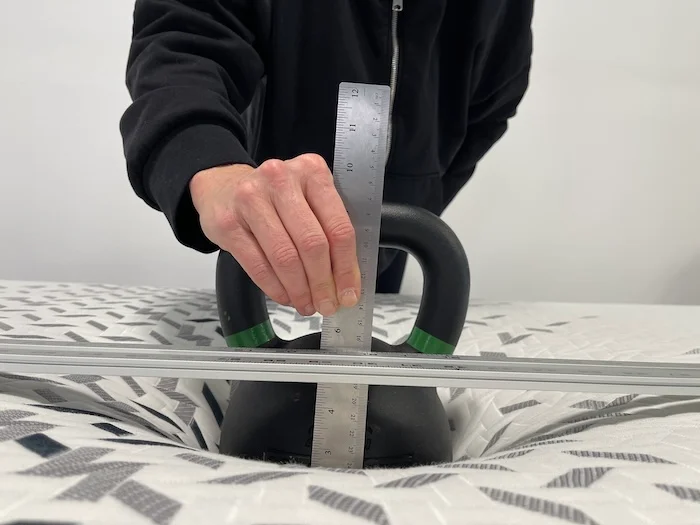 A kettlebell rests on the surface of the Nectar Luxe Memory foam. A woman is using a ruler to measure the sinkage.