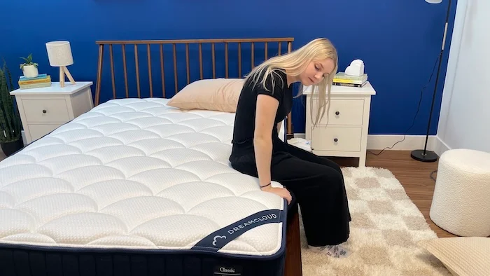 A woman sitting on the edge of the DreamCloud mattress.