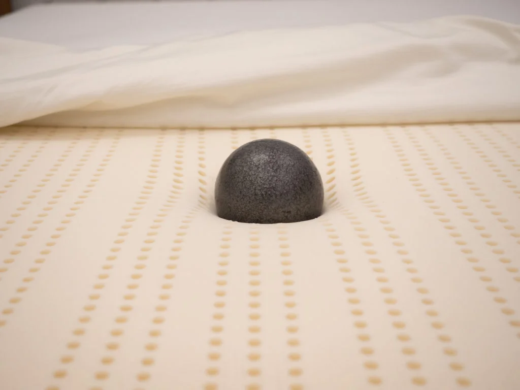 A steel ball resting on top of a mattress and slightly sinking into its layers.