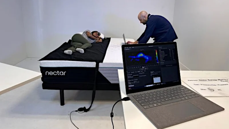 A woman lies on a pressure mat on the Nectar Premier mattress as a man types on his laptop on the other side of the bed