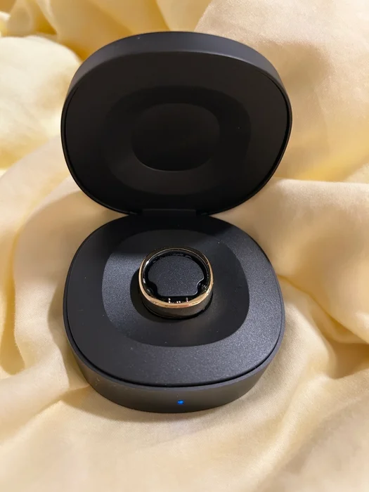 The wireless charging case for the RingConn 2 with the RingConn inside, sitting on a yellow cloth background.