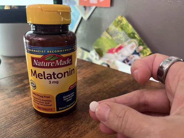 A hand holds a Nature Made Melatonin tablet.