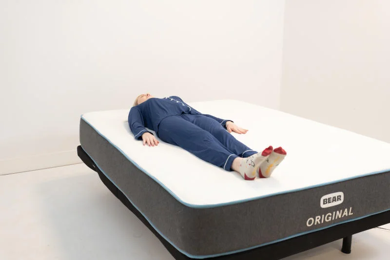 Sleep expert Riley Otis assessing the support of a Bear Original in a back-sleeping position.