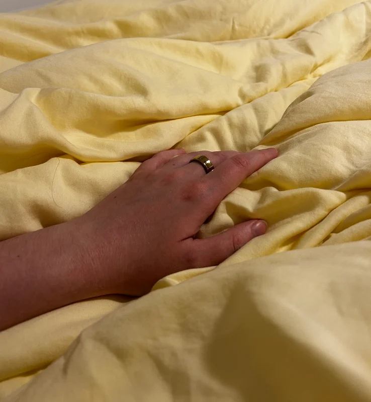 A hand rests on a yellow blanket displaying the RingConn ring on the middle finger.
