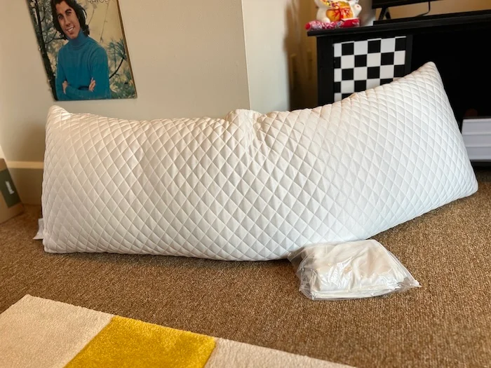 The Sleep Number Cool ComfortFit Body Pillow resting on the carpet.