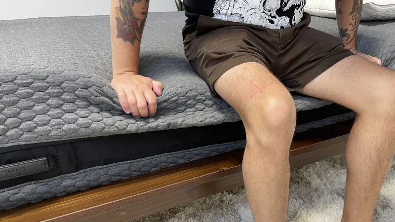 A person sits on the edge of a mattress