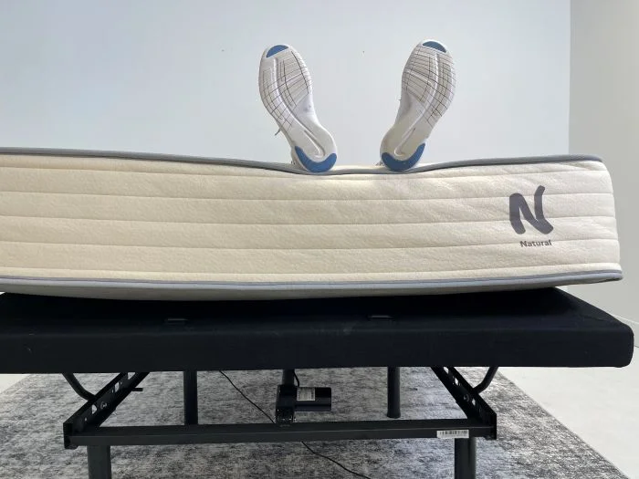A woman lying on a Nolah Natural mattress while it's on top of an adjustable base. Her feet are hanging off the bed.