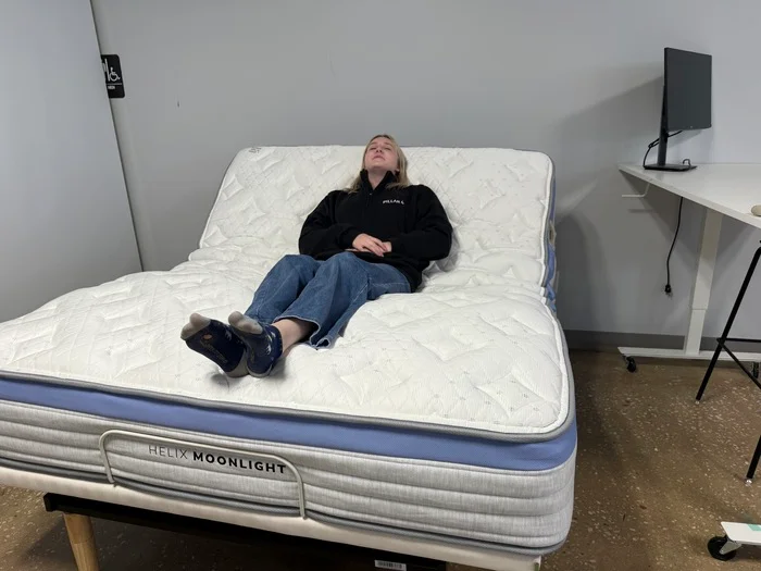 A woman sits on the Helix Moonlight mattress while reclining upright on an adjustable base