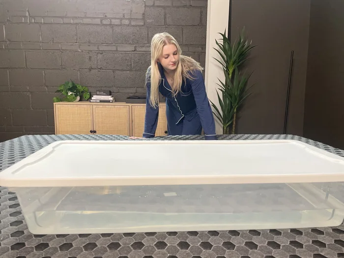 A woman standing next to a bin full of water on the firm side of the Layla mattress.