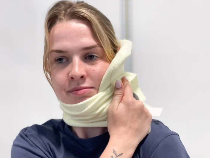 A woman wrapping a Trtl Travel Pillow around her neck.