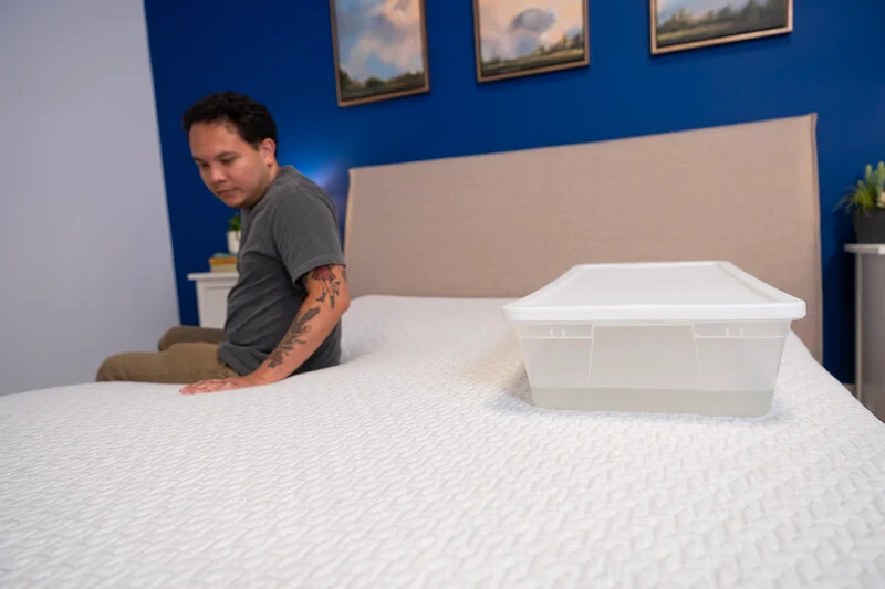 Kenny tests motion isolation by moving on the bed near a container filled with water