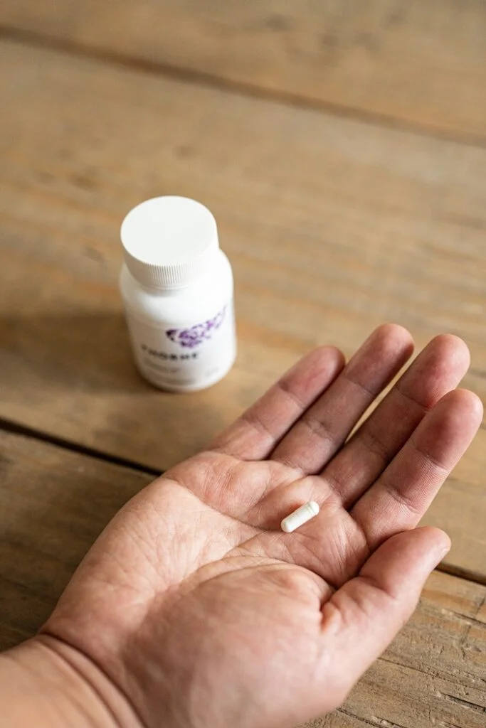 A hand holds a tiny Thorne Melatonin 5mg capsule.