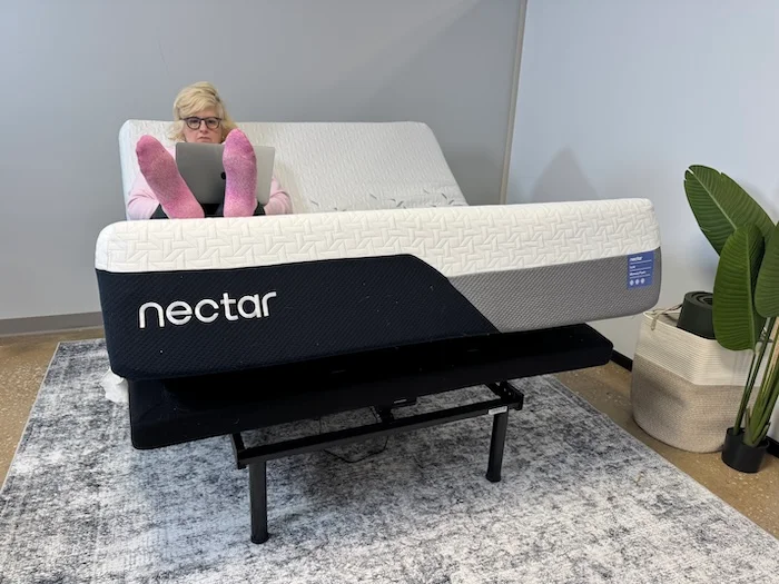 A woman sitting on the Nectar Luxe Memory foam mattress while it's on an adjustable base.