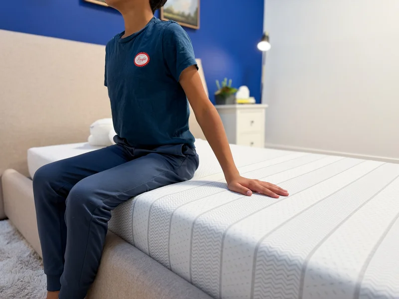 A tester sits on the side of the Leesa Kids mattress to test its edge support.