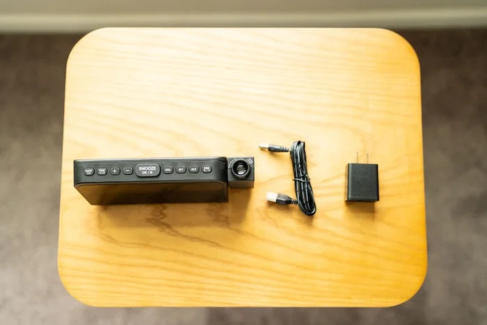 A top view of an unboxed Mesqool Projection Alarm Clock. Its cord is rolled up with a power block next to it.