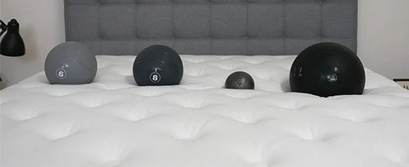 Four balls of different weights lined up on the surface of a mattress.