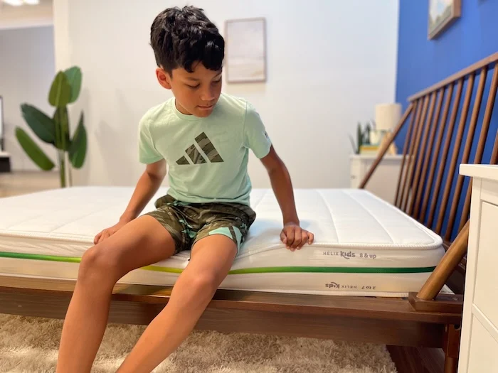 A 10-year-old boy sitting on the edge of the Helix Kids mattress.