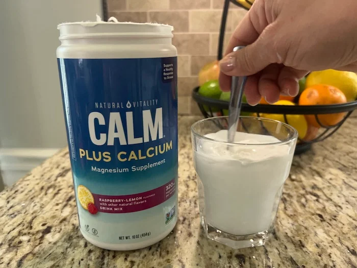 A hand stirring a glass of Natural Vitality Calm