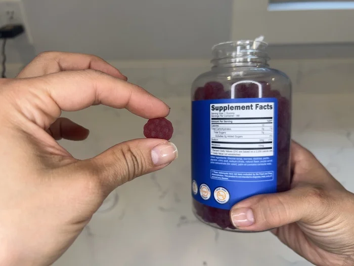A hand holds up a Nutricost Melatonin Sleep Gummy next to the Supplement Facts label.