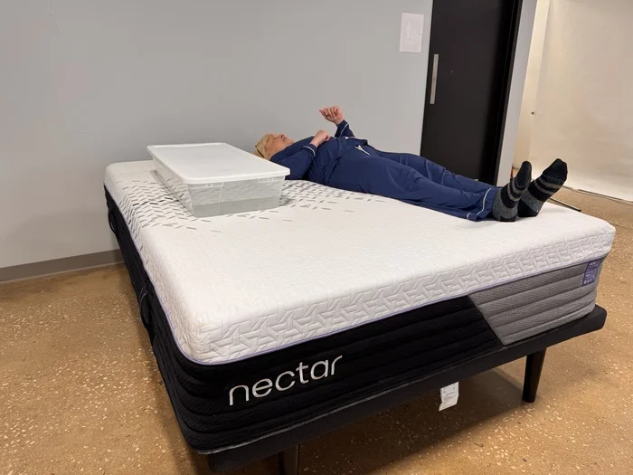 A woman lying on the Nectar Luxe Hybrid next to a plastic bin full of water. This is part of our ripple test, which measures motion isolation.