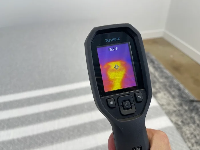 A closeup of someone using a thermal gun to read the temperature of the Leesa Original after 5 minutes of someone lying on the bed. The screen reads 70.2 degrees.