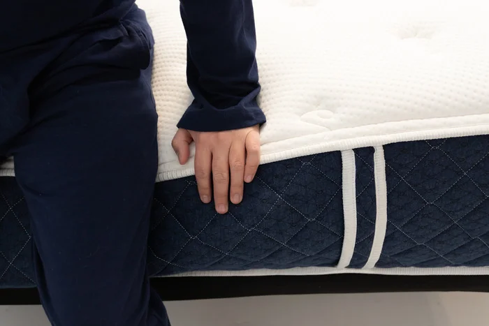 A closeup shot of someone sitting on the edge of the Brooklyn Bedding Signature Hybrid mattress and pressing into it with their hand.