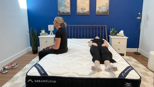 A woman sits on the edge of the DreamCloud mattress while another woman lies next to her.