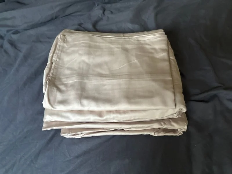 The Quince Bamboo sheet set folded and lying on a bed with a dark gray comforter in the background.